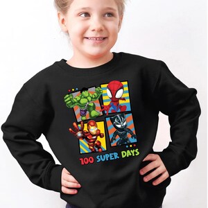 A young girl wearing a black sweatshirt with a graphic of four superhero characters: Hulk, Spider-Man, Black Widow, and Iron Man.