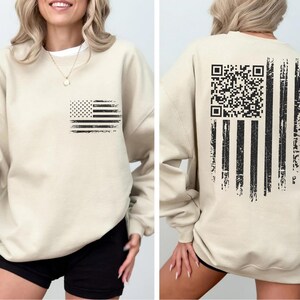 A woman wearing a beige sweatshirt with an American flag design and a QR code on the back.