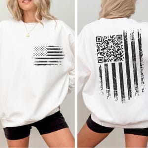 A white sweatshirt with a black graphic design on the back, depicting an American flag with a QR code.
