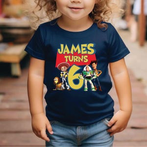 a little girl wearing a blue shirt with the name james turns 6 on it
