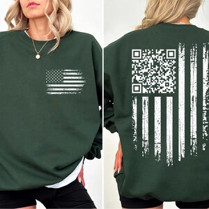 A woman wearing a green sweatshirt with an American flag design and a QR code printed on the back.