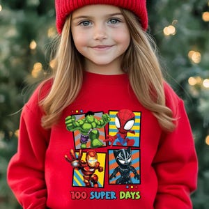 A young girl wearing a red beanie and a red sweater with a graphic of four cartoon characters: Hulk, Spider-Man, Iron Man, and Black Widow.
