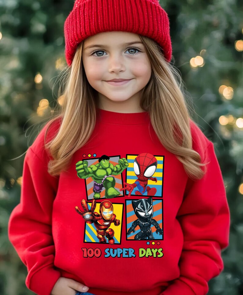 A young girl wearing a red beanie and a red sweater with a graphic of four cartoon characters: Hulk, Spider-Man, Iron Man, and Black Widow.