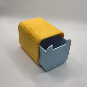 May include: A two-tone storage box with a yellow perforated top and a light blue drawer. The box has a rounded design and is set against a white background. The drawer is pulled out slightly.