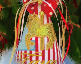 May include: A red and white striped party hat with a gold glitter carousel horse and the name "Faye" embroidered in gold. The hat is topped with a blue feather boa and a red bow with white polka dots.