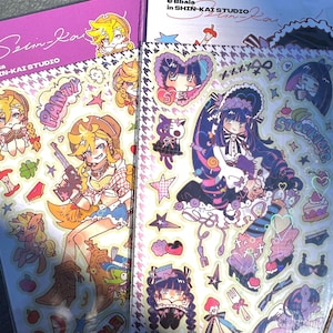 以下が含まれることがあります： アニメスタイルのイラストが描かれた2枚のステッカーシート。1枚はカウガールをテーマにした紫、もう1枚はゴシックロリータをテーマにした白です。どちらのシートにもホログラフィックアクセントと「Bbala in SHIN-KAI STUDIO」の文字が入っています。