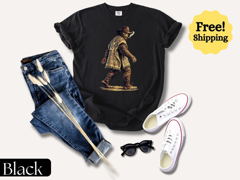 May include: Black t-shirt featuring a Bigfoot graphic wearing a poncho and cowboy hat. The image includes blue jeans, white sneakers, and black sunglasses. The word "Black" is displayed on a black rectangle.