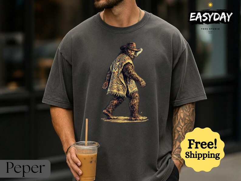 May include: Dark gray t-shirt featuring a Bigfoot illustration wearing a cowboy hat and poncho. The image includes the text "EASYDAY" and "Free! Shipping". The shirt is a relaxed fit.