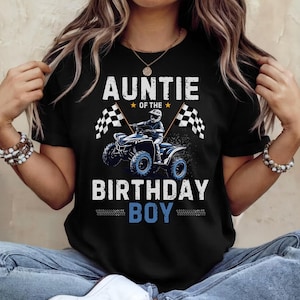 May include: Black t-shirt with the text "AUNTIE OF THE BIRTHDAY BOY" in white. The graphic features a blue ATV with a driver and checkered flags. The shirt is a crew neck and is being held up by a person.