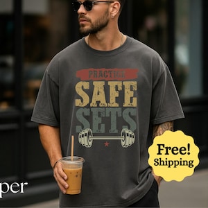 Könnte beinhalten: Dunkelgraues T-Shirt mit dem Text "PRACTICE SAFE SETS" in Retro-Schrift, mit einer Hantel-Grafik. Das Shirt hat einen Vintage-Look und -Feeling, geeignet für Fitnessstudio-Enthusiasten.
