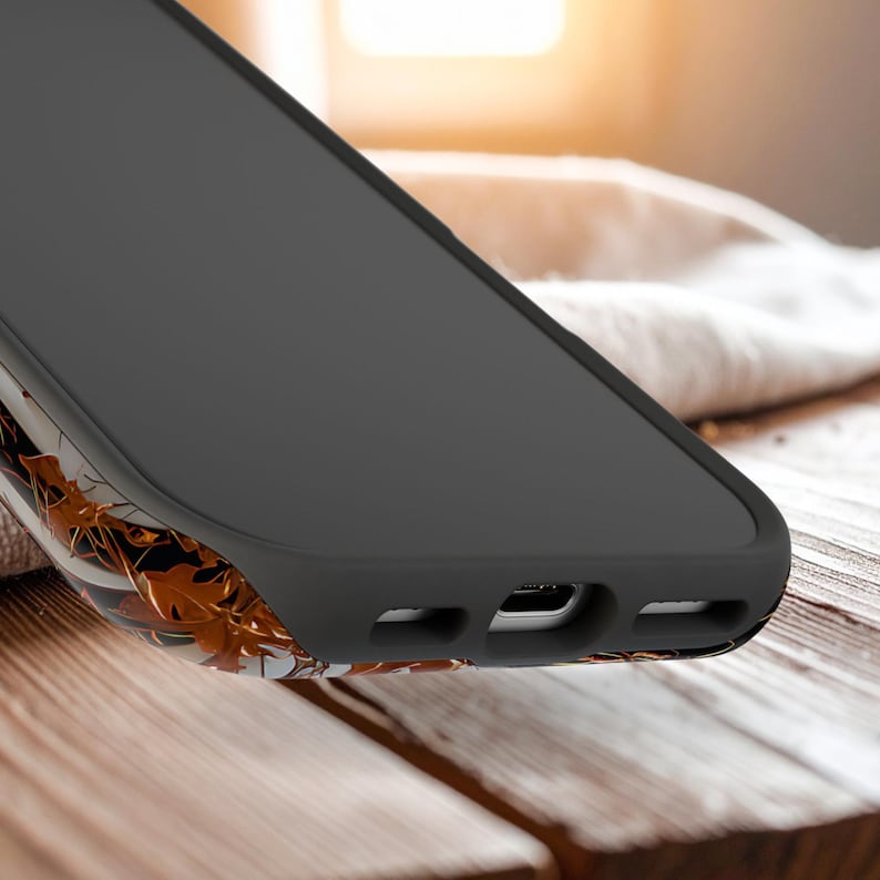 May include: Black phone case featuring a design of autumn leaves. The case has a black edge and a detailed pattern of brown and gold leaves. The phone's charging port and speaker are visible.