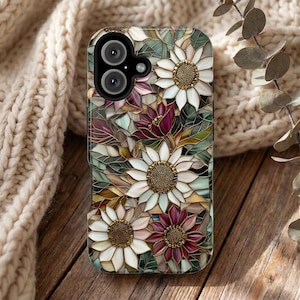 Puede incluir: Una funda para smartphone con un patrón de estilo vidriera de flores blancas y magenta intenso con centros dorados texturizados, intercaladas con elementos de follaje verde y marrón, rodeando un módulo de cámara dual negro arriba.