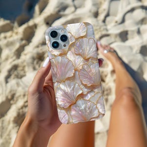 May include: A smartphone case featuring a layered, iridescent shell pattern with a pearlescent finish and gold-toned outlines. The design covers the entire back of the case, which includes a cutout for a triple-lens camera system on the top left.