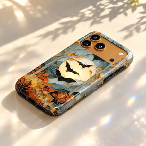 May include: A rectangular smartphone case featuring a stained-glass style design with a full moon, black bat silhouettes, and autumn-colored leaves in shades of orange and gold. The case has a gold-toned camera cutout area with three circular lenses.