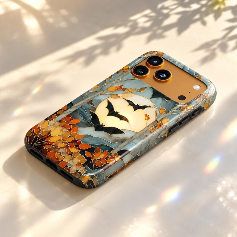 May include: A rectangular smartphone case featuring a stained-glass style design with a full moon, black bat silhouettes, and autumn-colored leaves in shades of orange and gold. The case has a gold-toned camera cutout area with three circular lenses.