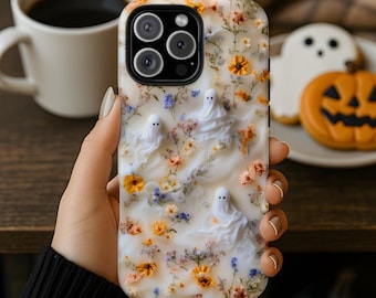 May include: A phone case featuring a white, marbled background decorated with small, pressed-style orange, yellow, and blue flowers. Three small, white, ghost-shaped figures are scattered across the surface, integrated into the floral design.