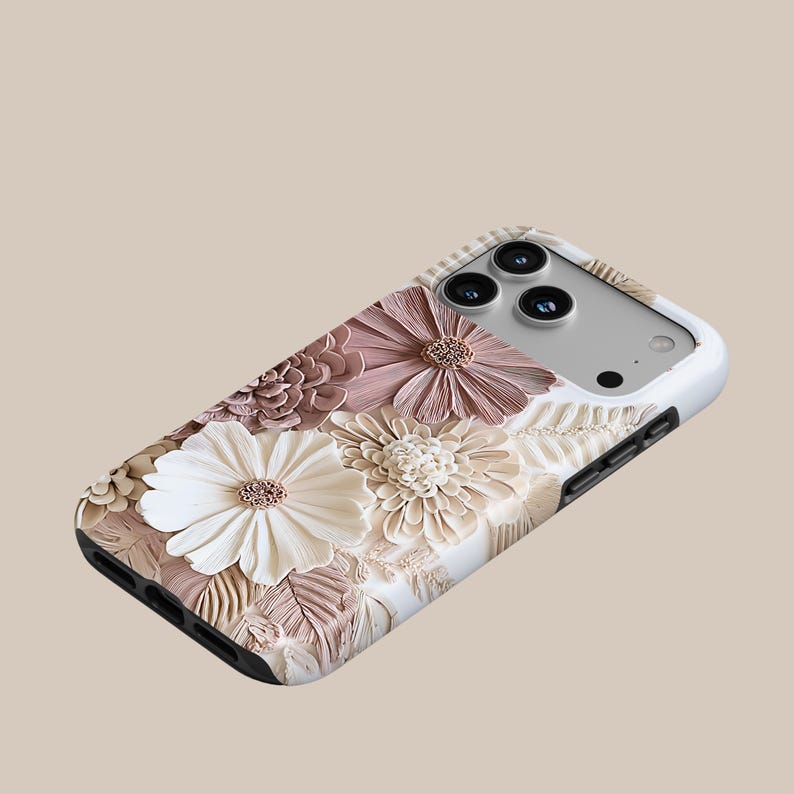 May include: A smartphone case featuring a three-dimensional floral design with layered petals in shades of white, cream, and dusty rose. The case has a white border, cutouts for the camera lenses, and a black edge along the bottom and side.