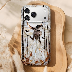 May include: A phone case with a witch design, wearing a black hat and white dress, set against a backdrop of bare trees and bats. The design incorporates gold and brown autumn leaves, creating a Halloween or autumn theme.