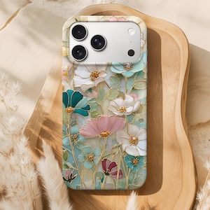 Puede incluir: Una funda de teléfono con un diseño floral en tonos pastel de rosa, turquesa y blanco. La funda tiene un acabado brillante y un borde dorado. La funda del teléfono está sobre una bandeja de madera.
