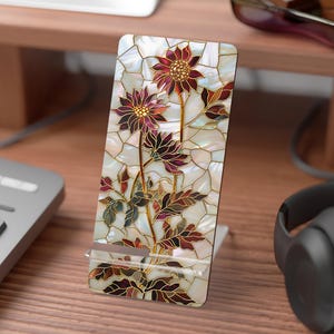 Op de afbeelding: Een rechthoekige telefoonstandaard met een bloemenontwerp. De standaard heeft een mozaïekachtig patroon met een parelmoer achtergrond en bordeauxrode, gouden en groene bloemen. De standaard is gemaakt van duurzaam materiaal en heeft een transparante kunststof voet.