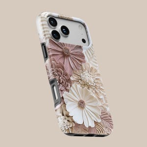 May include: A smartphone case featuring a three-dimensional floral design with layered petals in shades of dusty rose, cream, and beige. The case has a white frame, cutouts for the camera lenses, and side buttons, showcasing a textured botanical pattern.