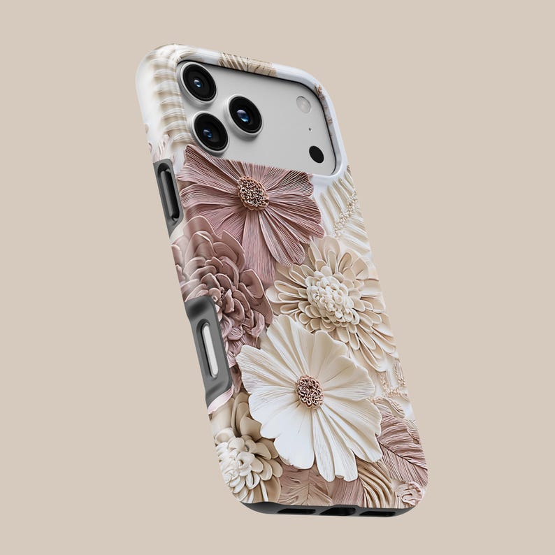 May include: A smartphone case featuring a three-dimensional floral design with layered petals in shades of dusty rose, cream, and beige. The case has a white frame, cutouts for the camera lenses, and side buttons, showcasing a textured botanical pattern.