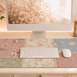 Peut inclure: Un tapis de bureau rectangulaire au motif patchwork matelassé avec divers imprimés floraux dans des tons de rose, bleu, vert et crème. Le tapis est posé sur un bureau blanc, accueillant un clavier sans fil blanc et une souris d'ordinateur blanche.