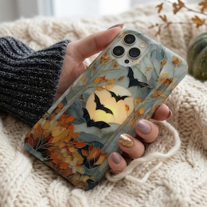 May include: A smartphone case featuring a stained-glass style design with a full moon, black silhouettes of flying bats, and autumn-colored foliage in shades of orange, yellow, and brown against a pale blue background with dark outlines.