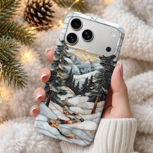 Puede incluir: Una funda para smartphone con un diseño estilo vidriera que muestra un paisaje montañoso nevado con pinos de color verde oscuro, suelo cubierto de nieve blanca y detalles en marrón claro, rodeando una triple cámara.