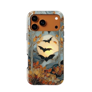 May include: A smartphone case featuring a stained glass style design of three black bats flying in front of a large, glowing yellow moon. The scene includes stylized trees with orange and brown autumn leaves, all outlined in thin gold lines.