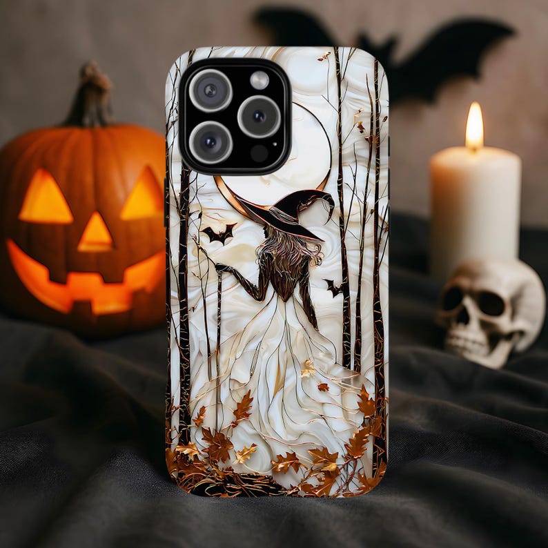 May include: A smartphone case with a witch illustration, a full moon, bats, and autumnal leaves. The witch wears a black hat and white dress. The case has a marble effect background with gold detailing. The case is designed for a mobile phone.