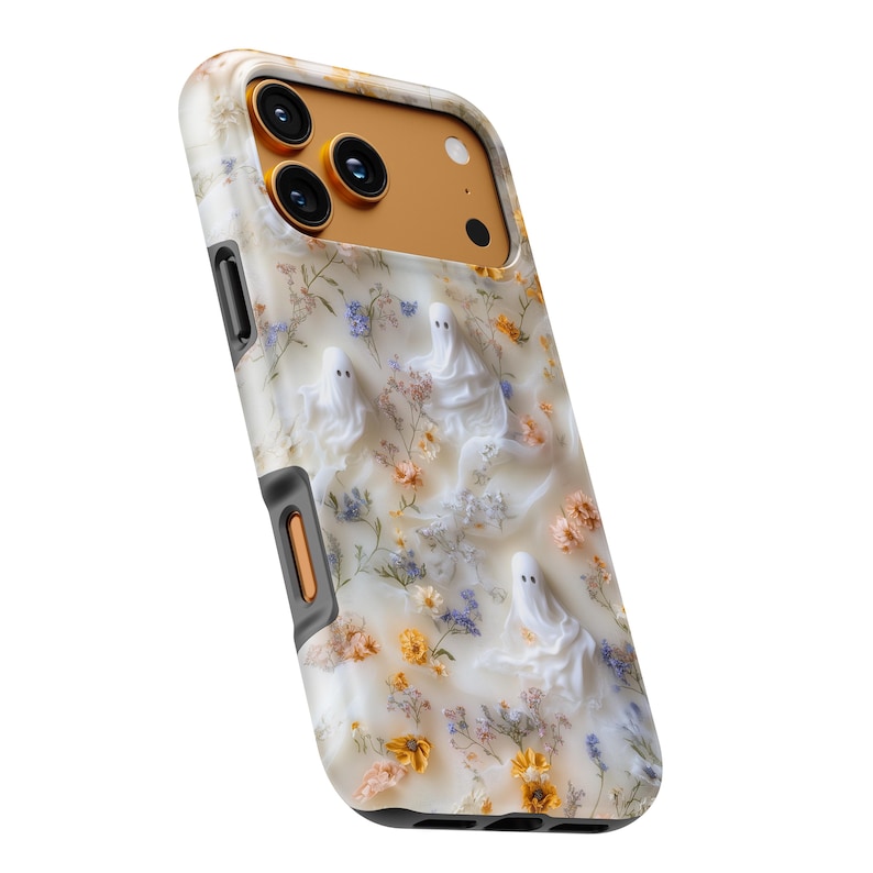 Puede incluir: Una funda para tel&eacute;fono con fondo color crema y un patr&oacute;n de peque&ntilde;as flores prensadas en tonos amarillos, naranjas y azules, intercaladas con tres figuras de fantasmas blancos. El &aacute;rea de la c&aacute;mara es de color dorado met&aacute;lico s&oacute;lido.
