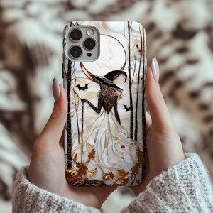 May include: A phone case with a witch illustration. The design includes a full moon, bats, and trees against a white backdrop. The witch is depicted in a black hat and white dress. The case has a glossy finish.
