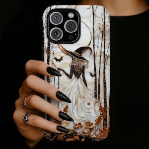 Puede incluir: Una funda de teléfono con una ilustración detallada de una figura con sombrero de ala ancha y vestido blanco fluido, de pie en un bosque de árboles oscuros bajo una gran luna. El diseño incluye pequeños murciélagos voladores y hojas de otoño doradas.