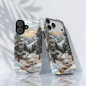 May include: Two phone cases featuring a stained glass style design of a winter landscape with snow-covered ground, dark evergreen trees, and distant mountains in shades of white, gray, and amber, with cutouts for the camera lenses and buttons.