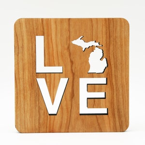 Könnte beinhalten: Ein Holzschild mit dem Wort "LOVE" und einer Umrandung des Bundesstaates Michigan. Das Schild ist aus Naturholz mit einer hellbraunen Oberfläche.