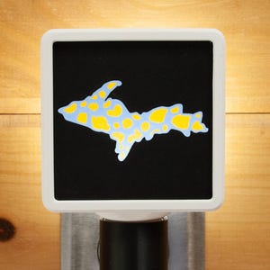 Peut inclure: Veilleuse avec un carré noir orné d'une carte bleu clair et jaune de la péninsule supérieure du Michigan. La veilleuse a un cadre carré blanc et une base noire.
