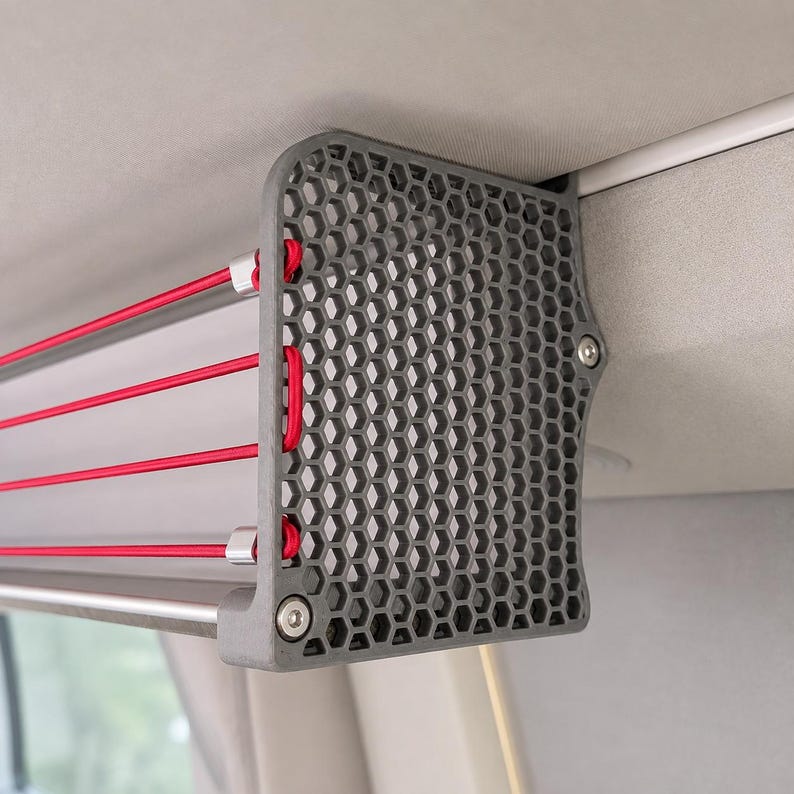 Seitenansicht: VW California Deckenregal für T5, T5.1, T6 und T6.1 im Camper-Innenraum. Dachablage mit grauen Seitenteilen, roten Gummibändern und Aluminiumstange, montiert an der seitlichen Dachschiene für zusätzlichen Stauraum.