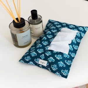 May include: A teal fabric tissue holder with a white leaf pattern and a small white label reading Lovingness, accompanied by a glass home fragrance diffuser with wooden reeds and a clear glass bottle with a black cap and a white label.