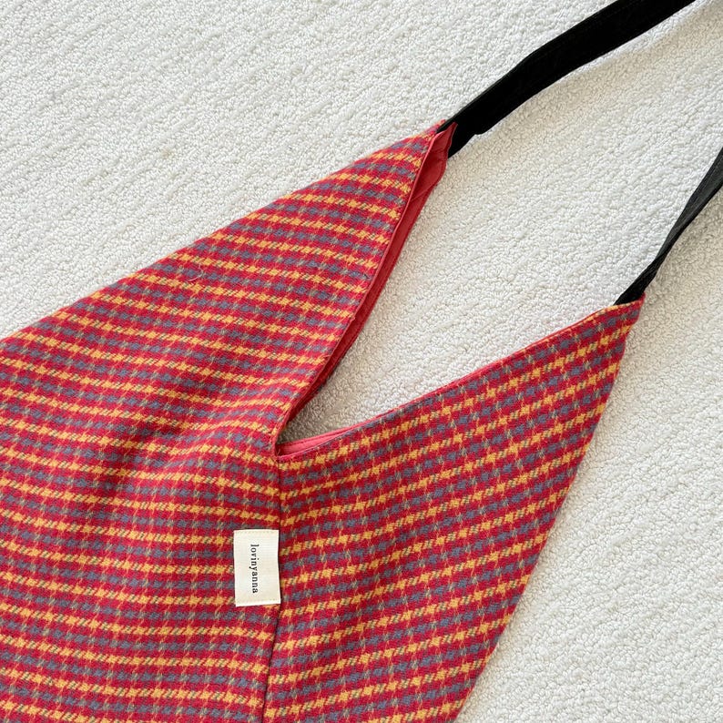 Puede incluir: Bolso de hombro a cuadros rojos y amarillos con una correa negra. El bolso tiene una forma triangular &uacute;nica y una peque&ntilde;a etiqueta blanca con el texto "lovingyana". El bolso est&aacute; hecho de tela tejida.