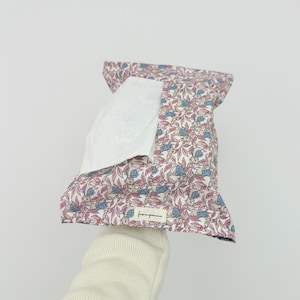 Peut inclure: Un étui à mouchoirs en tissu avec un motif répétitif de petits lapins et de feuilles roses sur fond blanc. L'étui présente un mouchoir blanc partiellement sorti et une petite étiquette rectangulaire avec le texte lovinganna cousu devant.