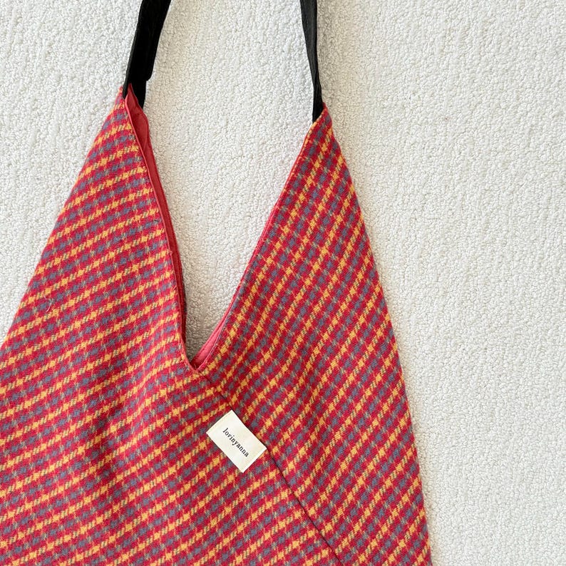 Puede incluir: Un bolso tote con estampado rojo y amarillo con una correa negra. El bolso tiene una forma triangular &uacute;nica y una peque&ntilde;a etiqueta que dice "loriyanna". El interior de la bolsa es rojo.