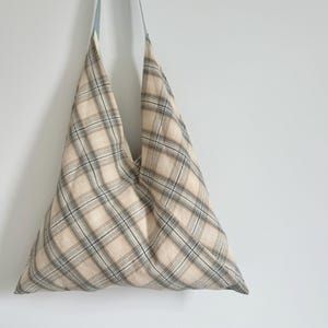 Könnte beinhalten: Eine beige und braune karierte Tragetasche mit einem hellblauen Riemen.