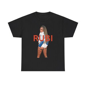 Peut inclure: T-shirt noir avec le texte "RUBI" en rouge et une photo d'une femme portant une tenue blanche et bleue.