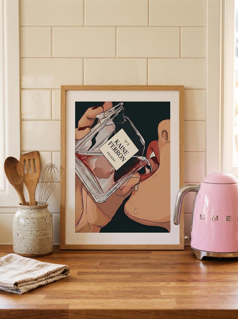 May include: Framed art print featuring a stylized illustration of a person drinking from a perfume bottle. The bottle is labeled "KAINE FERRON PALADIA N&deg;3". The artwork has a dark background and is set in a kitchen with a pink kettle.