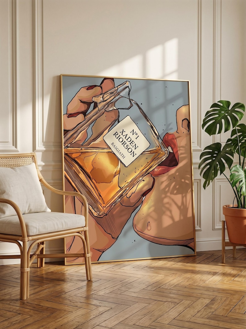 Pode incluir: Ilustra&ccedil;&atilde;o de uma pessoa bebendo de um frasco de perfume. A garrafa est&aacute; rotulada como "N&deg;1 Xaden Riorso Basgiath". A obra de arte &eacute; emoldurada em ouro e pendurada em uma parede. Uma planta em vaso e uma cadeira de vime est&atilde;o em primeiro plano.