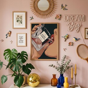 May include: Aesthetic wall decor featuring a framed print of a person drinking perfume, a round mirror, and a neon "Dream Big" sign. Decorative elements include faux birds, flowers, and a disco ball. The color scheme is primarily pink, gold, and green.