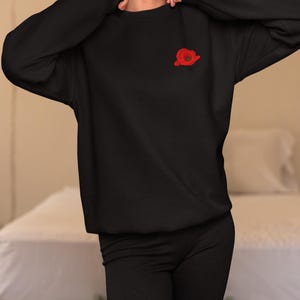 May include: A black sweatshirt with a red poppy embroidered on the left chest.