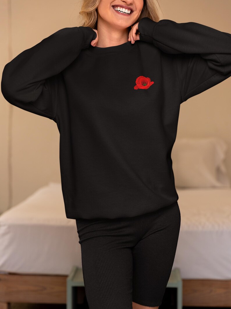 May include: A black sweatshirt with a red poppy embroidered on the left chest.
