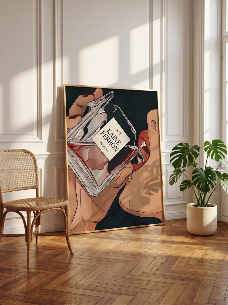 May include: A framed art print featuring a stylized illustration of a perfume bottle labeled "KAINE FERRON PALADIA" being held near a person's lips. The artwork has a dark background and a gold frame, with a neutral-toned interior setting.